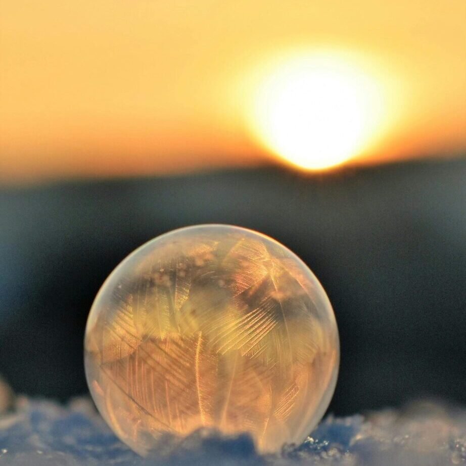 A frozen soap bubble on snow captures crystalline patterns against a sunrise backdrop.