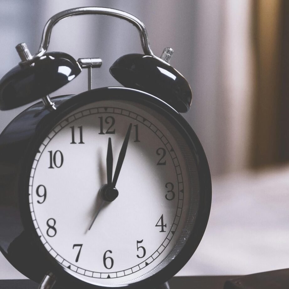 A classic analog alarm clock on a modern desk setup with a laptop and pens, creating a balanced workspace vibe.